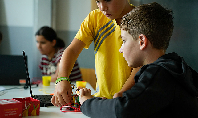 2 Kinder tüfteln an Steckverbindungen an einem Notebook